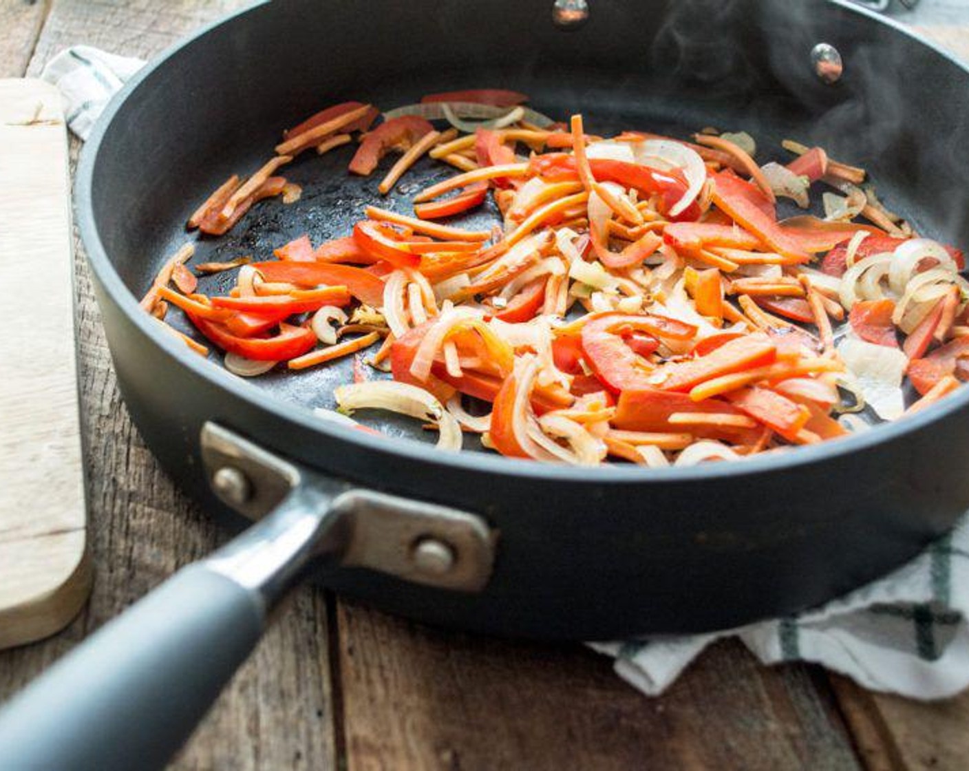 Schritt 4 In den letzen 10 Minuten bevor der Kürbis gar ist, Peperoni (2/3), Zwiebel (70 g) und Karotten (75 g) in eine grosse Pfanne geben und bei mittlerer Hitze 3-5 Minuten andünsten.