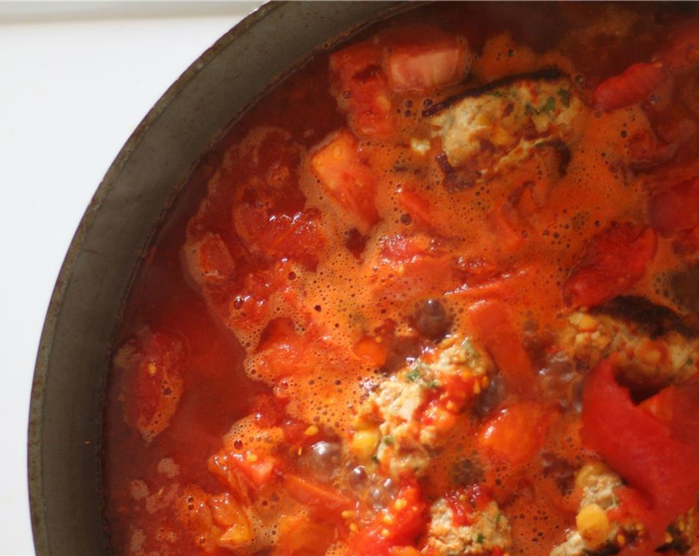 Schritt 4 Auf mittlere bis hohe Hitze herunterschalten und Tomaten (2) hinzugeben. Ein paar Minuten weich werden lassen und dann die Pelati Pomodoro (1 Dose) und die Hühnerfond (240 ml) hinzufügen. Die Flüssigkeit sollte die Fleischbällchen fast vollständig bedecken.