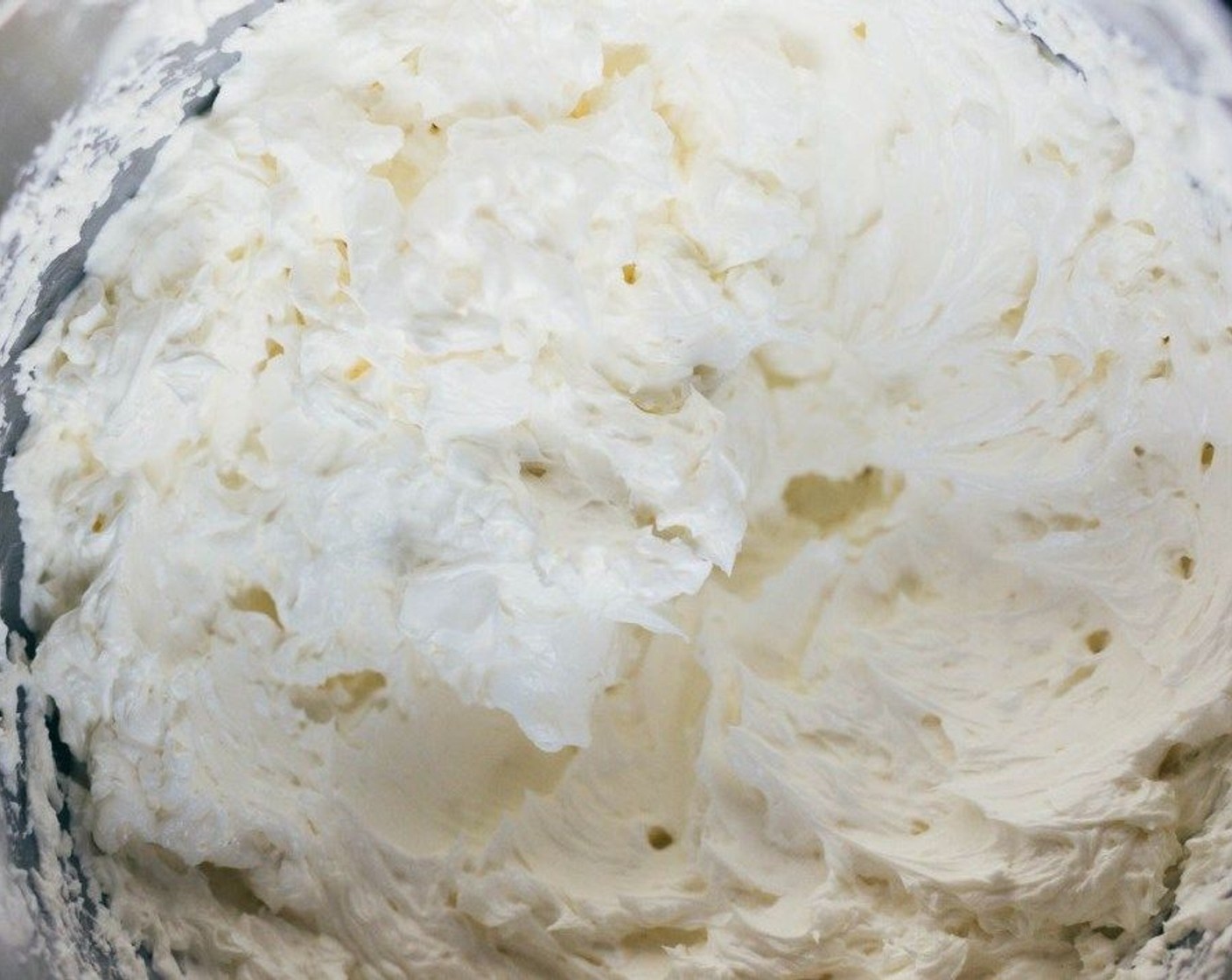 Schritt 5 Vanille (2 Teelöffel) esslöffelweise hinzugeben, während der Mixer auf niedriger/mittlerer Geschwindigkeit weiter läuft. Die Mischung wird sich zunächst verflüssigen und dann fester werden. Butter (4 Esslöffel) hinzugeben. Sobald die Butter vollständig eingearbeitet ist, noch 1 bis 2 Minuten auf höchster Stufe weiterrühren.