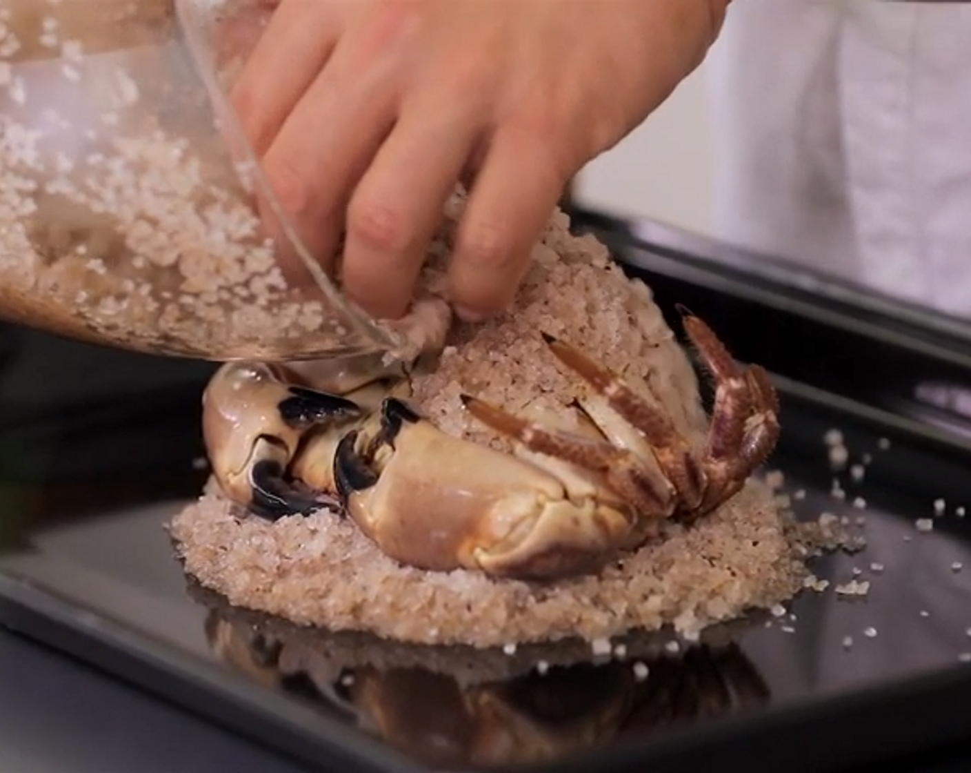 Schritt 3 In einer Schüssel das Salz, grobkörnig (1 kg) und Fünf-Gewürz-Pulver (1 TL) mischen. Dann das Wasser (600 ml) hinzufügen. Ein Viertel des gewürzten Salzes auf ein mit Backpapier belegtes Blech geben, in der Grösse der Krabbe verteilen und flach drücken. Krabbe mit der Bauchseite nach oben auf das Salz legen, mit dem restlichen Gewürzsalz bedecken und leicht andrücken.