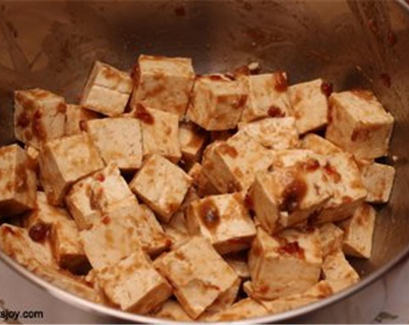 Schritt 3 Den Tofuwürfel dazugeben und gut vermengen, sodass jeder Würfel mit Marinade bedeckt ist. Das Ganze etwa 30 Minuten bis zu einer Stunde ruhen lassen. Dann den Backofen auf 175 °C vorheizen.
