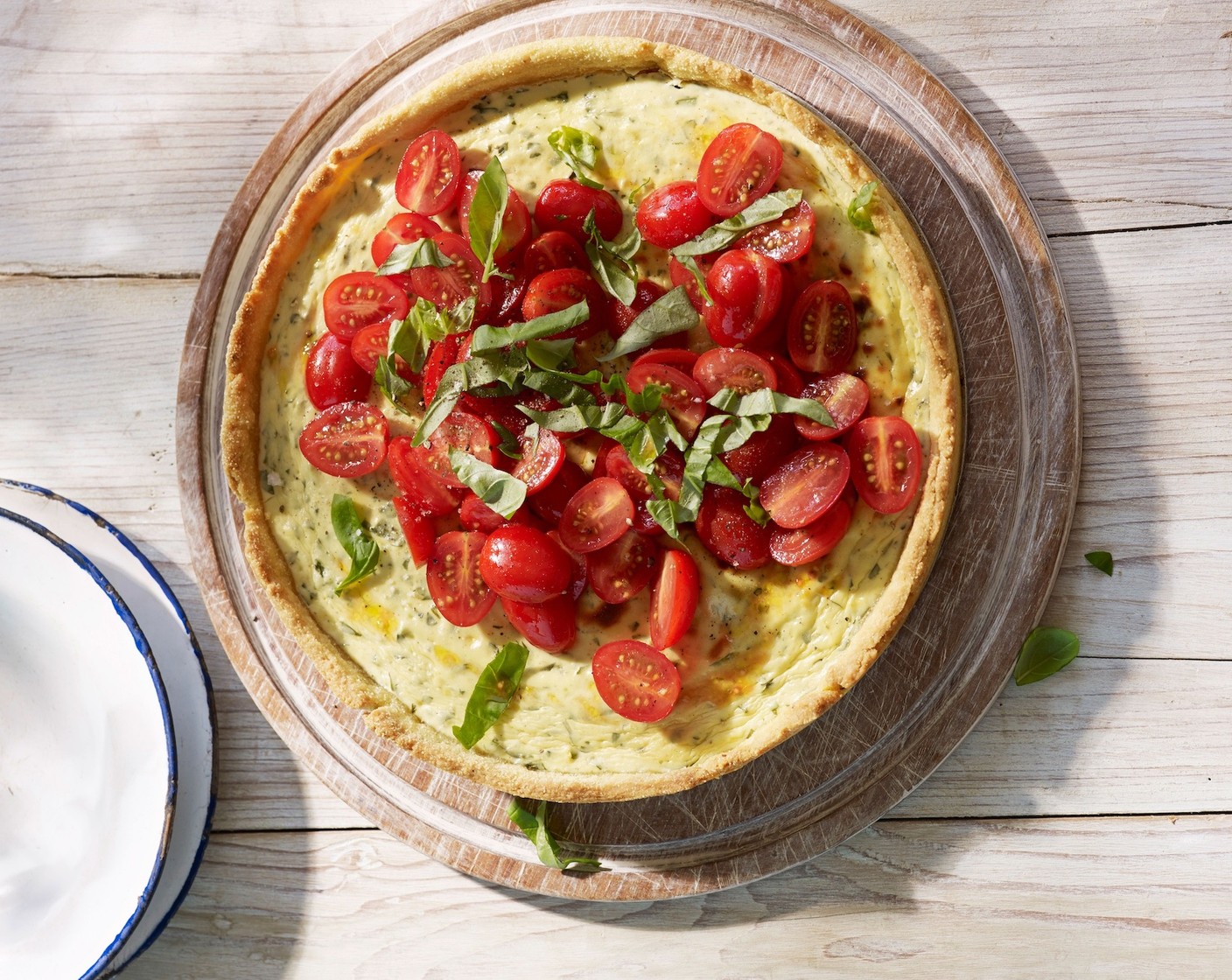 Schritt 6 Für den Belag Tomaten (250 g) halbieren und in eine Schüssel geben. Olivenöl (2 Esslöffel) daruntermischen, mit Fleur de Sel (1/4) und Pfeffer (wenig) würzen. Tomaten auf dem Belag verteilen. Restliches Basilikum darüber zupfen.