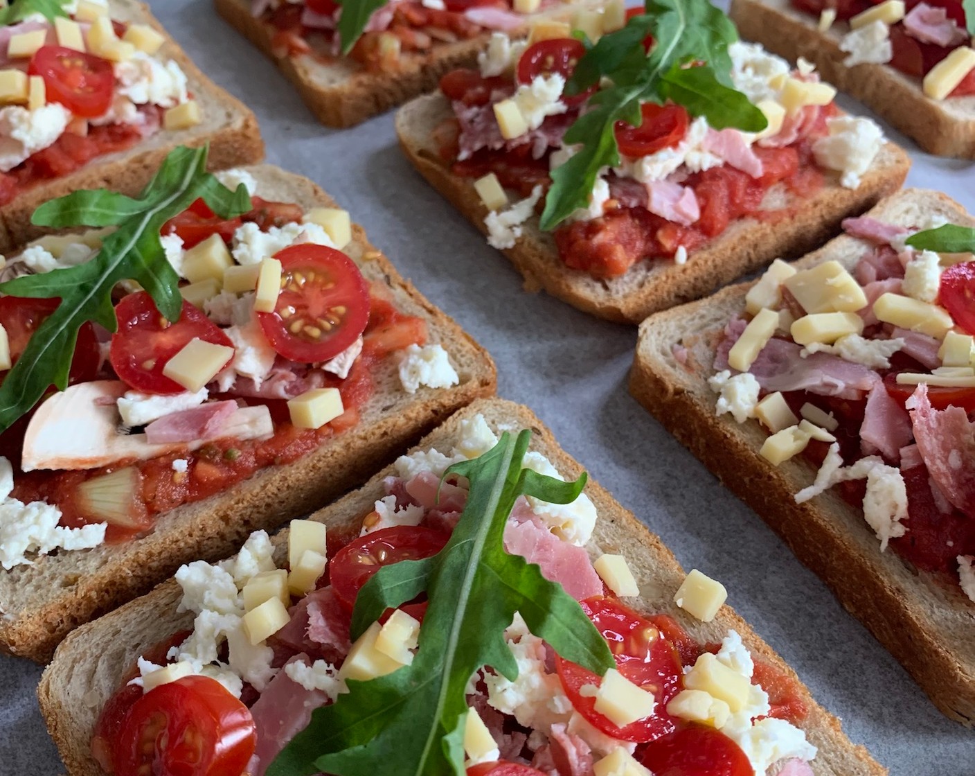 Schritt 4 Als nächstes den Mozzarella (1 Kugel) zerbröseln und in eine Schüssel geben. Den Raclettekäse (2 Scheiben) würfeln und mit dem Mozzarella vermengen. Den Käse-Mix auf den Toasts verteilen und mit Rucola (1 Handvoll) belegen.