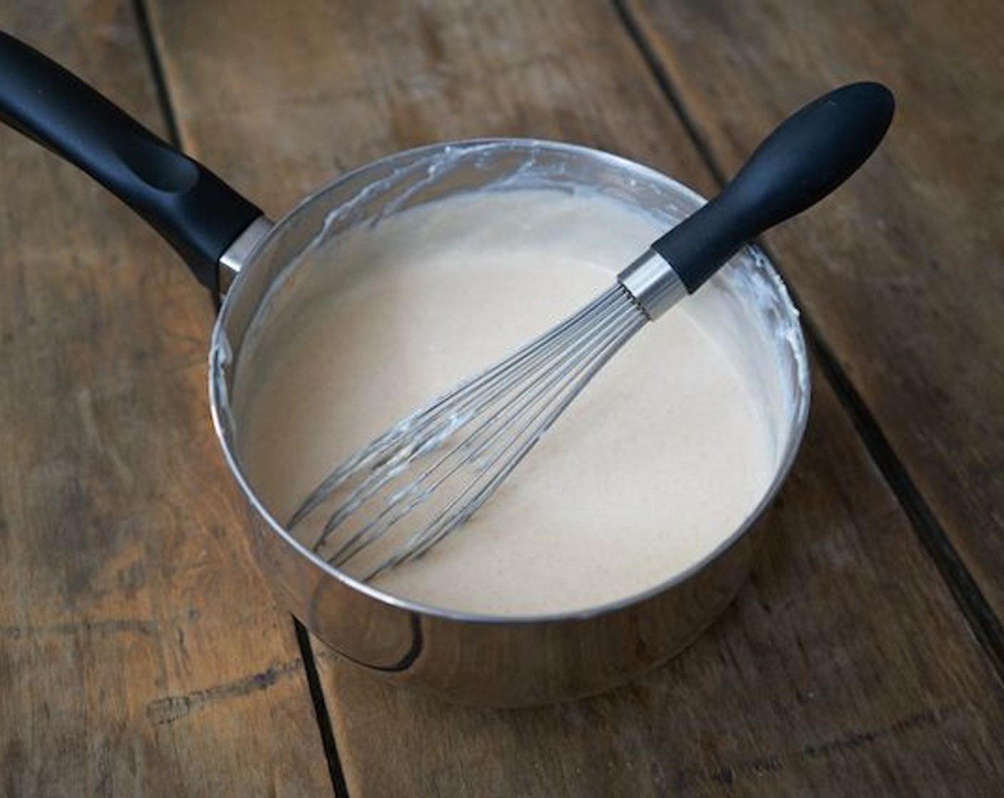 Schritt 7 Nach und nach die Milch hinzufügen und dabei ständig rühren, um Klumpen zu vermeiden. Sobald die gesamte Milch eingearbeitet ist, die Masse zum Kochen bringen und gelegentlich weiterschlagen, bis sie eindickt (4-5 Minuten).