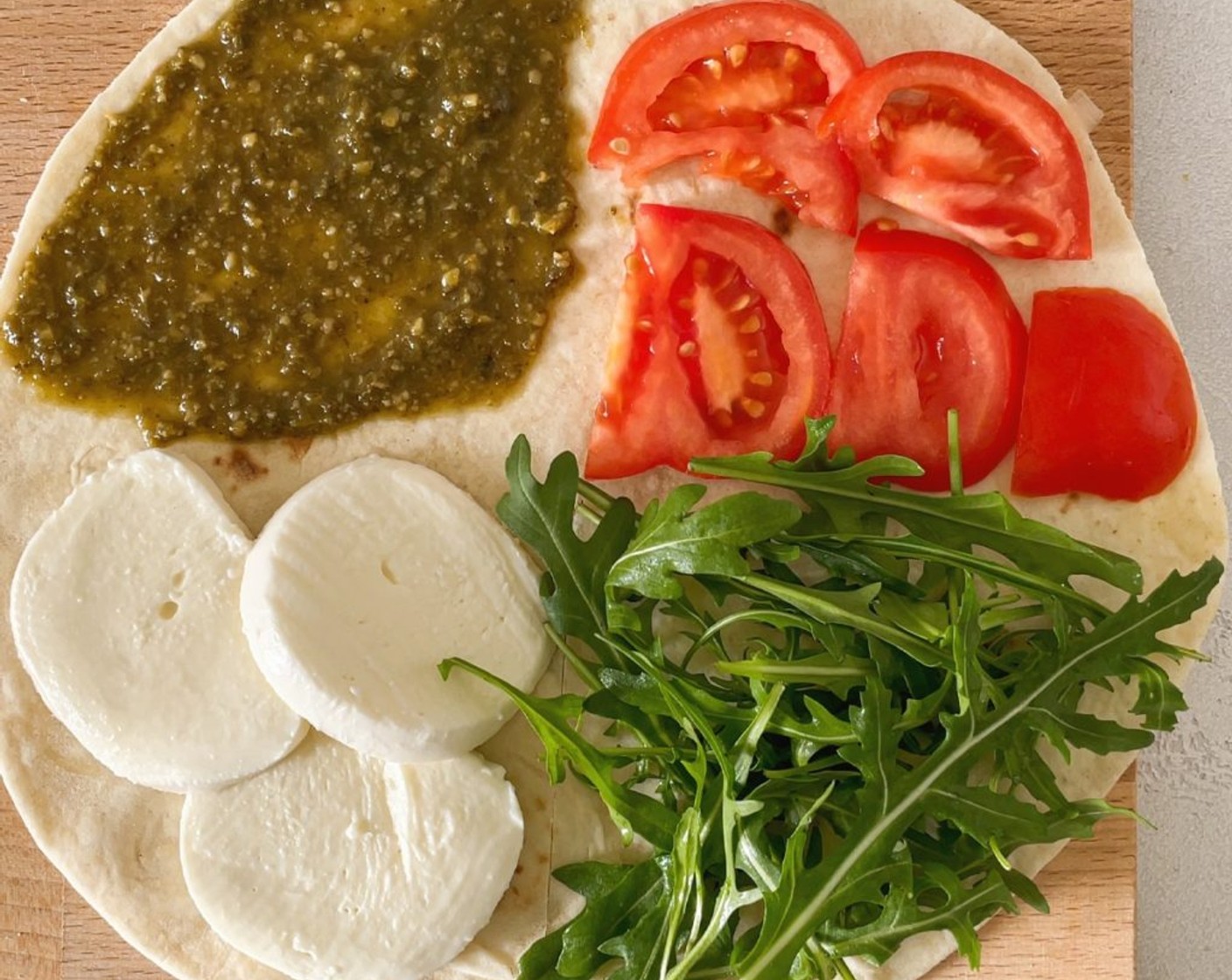 Schritt 4 Die Zutaten gleichmässig auf die Wraps aufteilen und im Uhrzeigersinn viertelweise belegen. Das erste Viertel mit dem Pesto (1/4 Ta.) bestreichen, die nächste Viertel mit Tomaten und Rucola belegen und auf das letzte Viertel den Mozzarella geben.