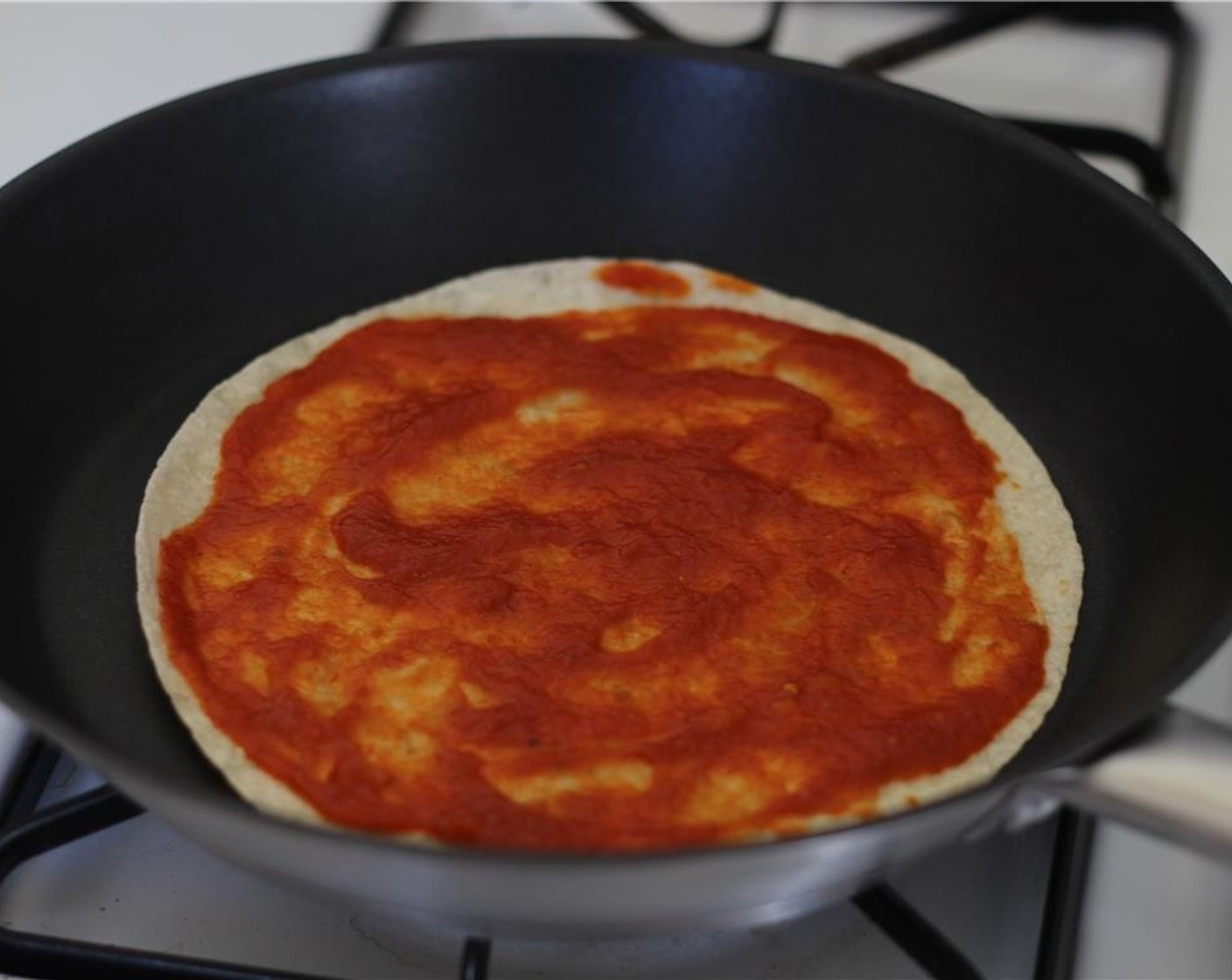 Schritt 1 1 Tortilla (2) in eine heisse Pfanne legen und Marinara Sauce (2 Esslöffel) darauf verteilen.