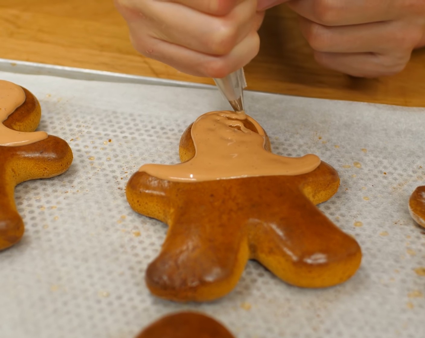 Schritt 20 Die Lebkuchen-Männchen mit dem Kopf nach unten vor sich hinlegen. Danach mit dem Royal Icing den Rand des Kopfes und bis etwa in die Hälfte der Arme bespritzen, so dass die Schnauze des Rentieres entsteht. Diese Markierung vorsichtig mit Royal Icing ausfüllen. Tipp: Sollte das Royal Icing zu fest sein, ein paar wenige Tropfen Wasser darunter rühren.