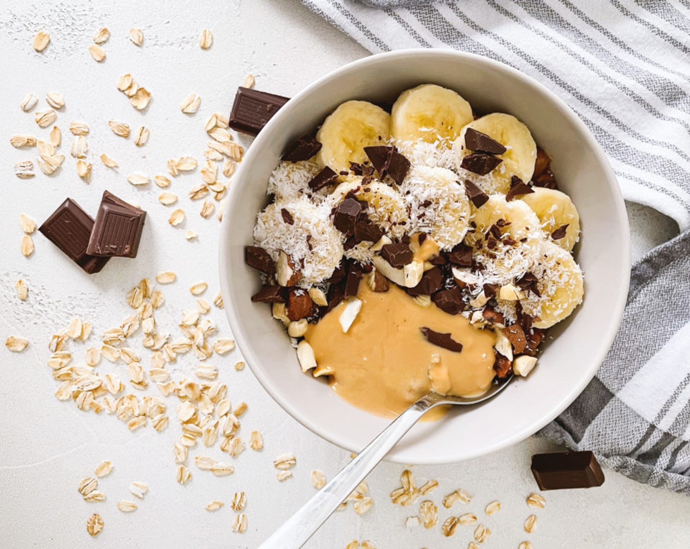 Schritt 2 Den Mix in eine Schüssel geben, die beiseitegelegte Banane (1/2) in Scheiben schneiden und auf dem Oatmeal-Mix anrichten. Dann mit Schokolade (2 Stück), Erdnussbutter (1 TL), Nüssen (1 EL) und Kokosraspeln (1 EL) ausgarnieren.