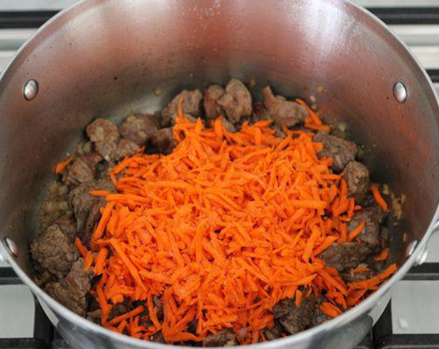 Schritt 4 Geraspelte Karotten (3) hinzufügen und mit Chili (1 TL), Salz (wenig) und Pfeffer (wenig) würzen. Wieder zudecken und bei mittlerer Hitze kochen, bis die Karotten weich sind.