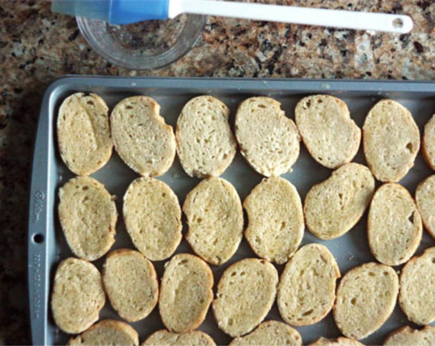 Schritt 5 Ein Backblech in die Mitte des Ofens schieben und diesen im Grill-Modus auf höchster Stufe vorheizen. Baguette (1/2) in Scheiben schneiden und die Scheiben in einer einzigen Lage auf dem Backblech ausbreiten. Butter (4 Esslöffel) schmelzen und über jedes Brot streichen.