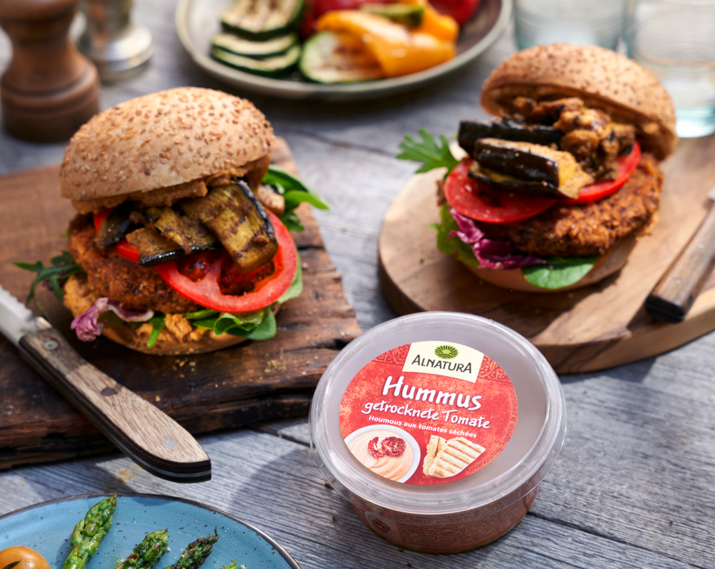 Schritt 6 Burgerbrötchen (4) halbieren und mit der Schnittseite auf dem Grill rösten. Die Unter- und Oberseite jedes Brötchens mit Hummus (150 g) bestreichen, dann die Unterseite mit Salat-Mix belegen und darauf Burger-Patty, Tomatenscheibe und die gezupften Auberginen schichten.