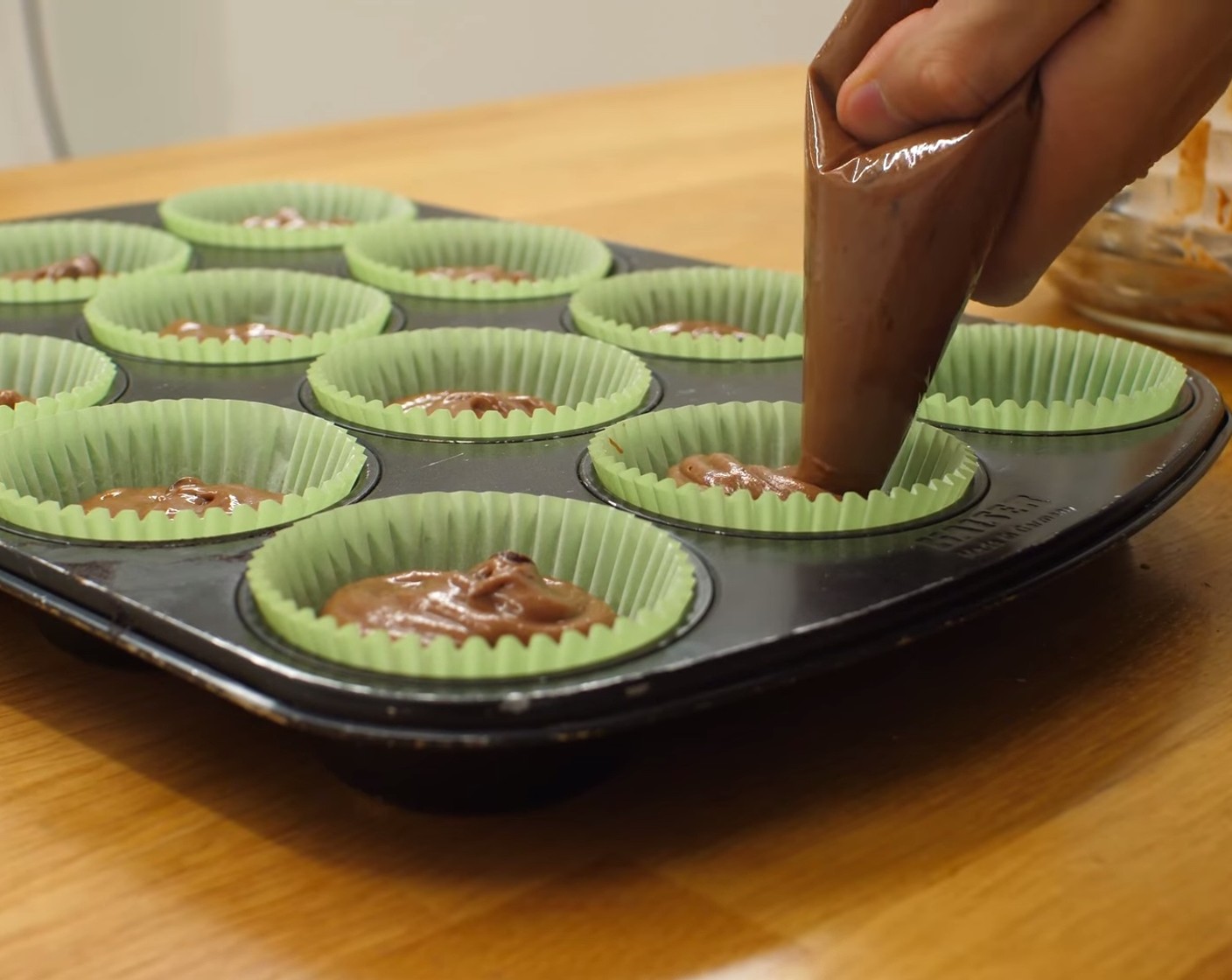 Schritt 8 Als nächstes das Muffinblech mit Papierförmchen auslegen. Den Teig entweder in einen Spritzbeutel füllen oder mit zwei Löffeln auf die Papierförmchen verteilen. Nach dem Befüllen, das Blech ein paar Mal auf die Arbeitsfläche klopfen, um Hohlräume zu füllen und um die Masse besser zu verteilen.