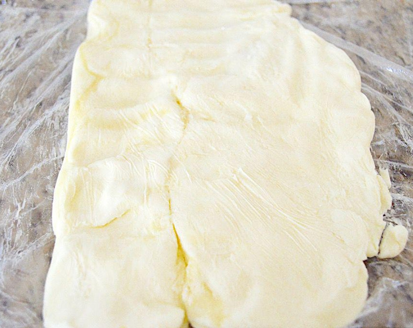 Schritt 5 Sobald der Teig fertig ist, wird die Butterplatte geformt.
Ein grosses Stück Frischhaltefolie auslegen und leicht bemehlen. Die weiche Butter (300 g) auf eine Hälfte davon legen und auch die Oberseite der Butter mit Mehl bestäuben. Die andere Hälfte der Folie darüberlegen und leicht mit den Händen zu einem dünnen Rechteck zwischen der Folie drücken. In den Kühlschrank legen, damit es wieder fest wird.